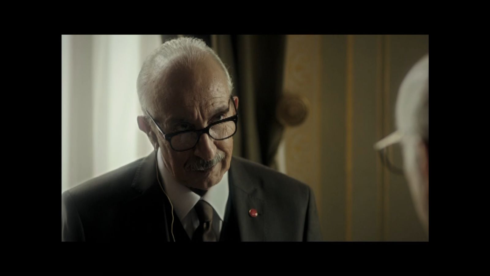 Ben Onu Çok Sevdim — A grey-haired man in glasses and a dark suit beside a window.