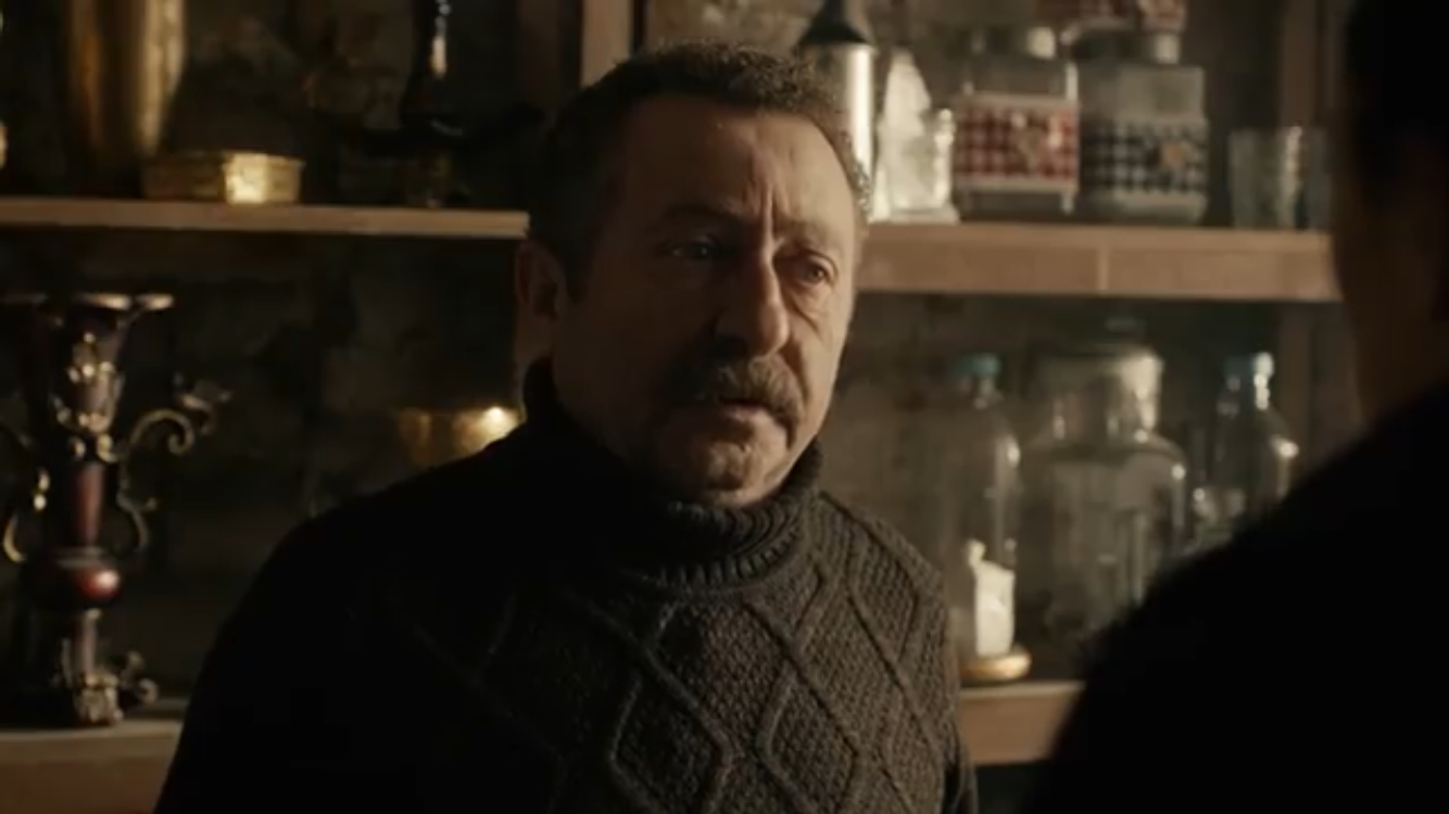Bir Deli Sevda — A man seated among shelves of glassware.