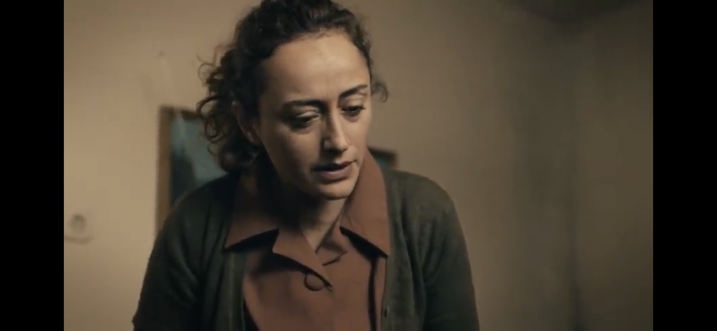 Bir Deli Sevda — A woman looking down in a warmly lit room.