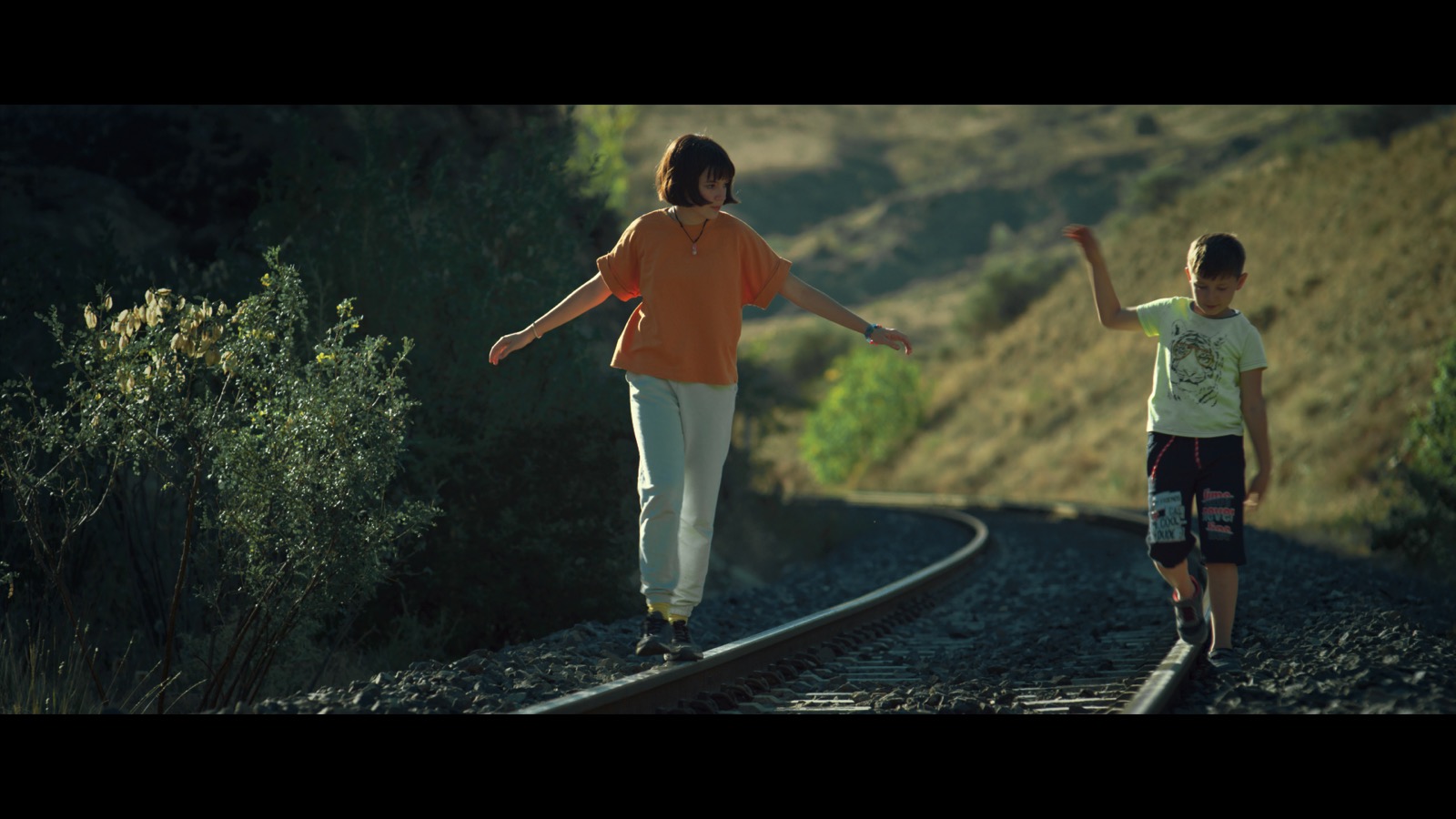 Kabahat — Two children balancing on railway tracks in afternoon light.