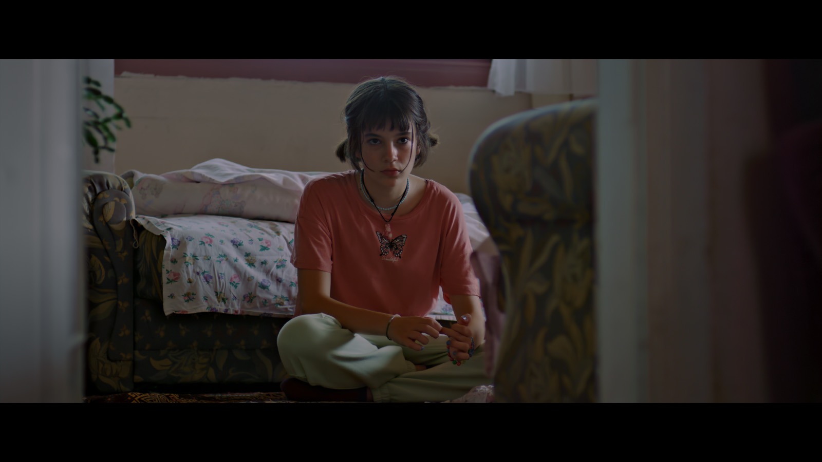 Kabahat — A girl sitting on the floor beside a patterned sofa.