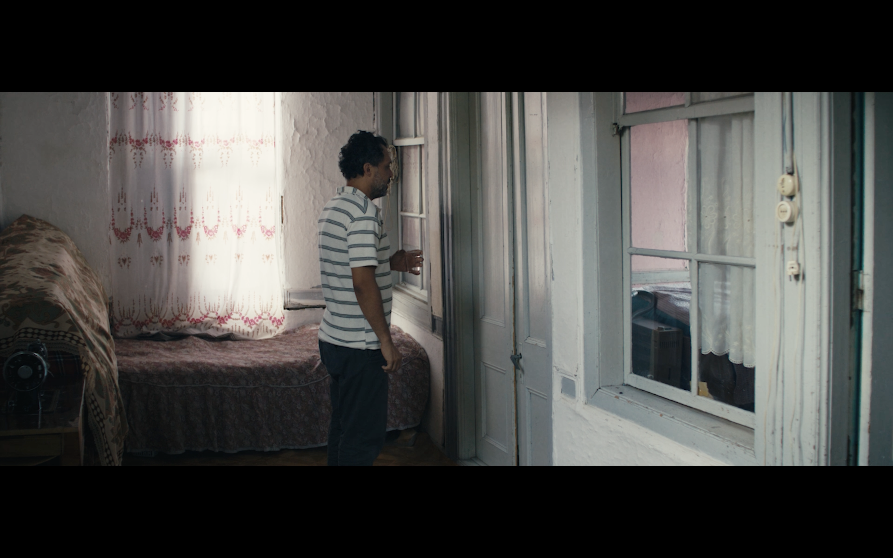 Kavanoz — A man standing beside glass-panelled doors in a softly lit room.