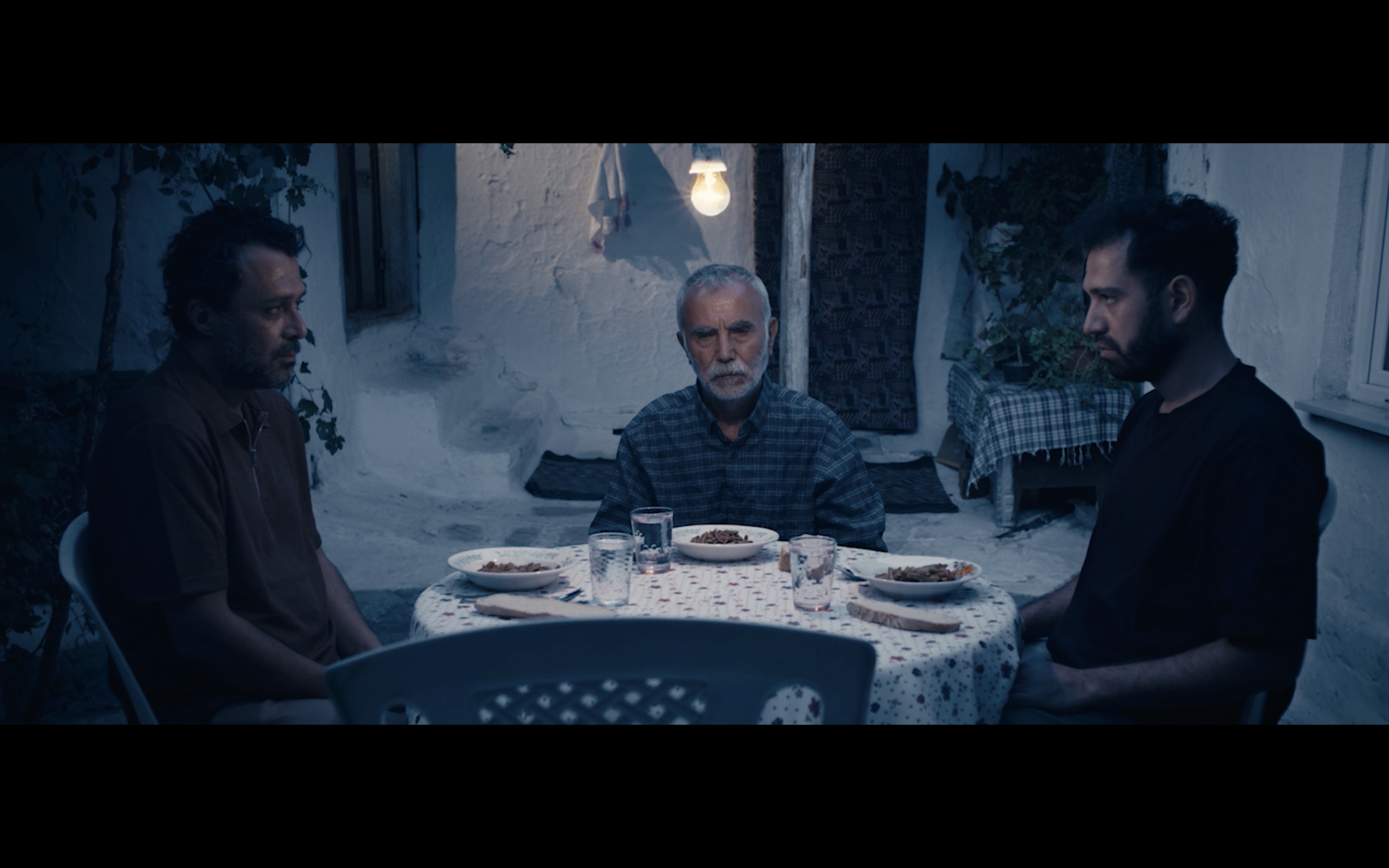 Kavanoz — Three men seated around an outdoor table at night.
