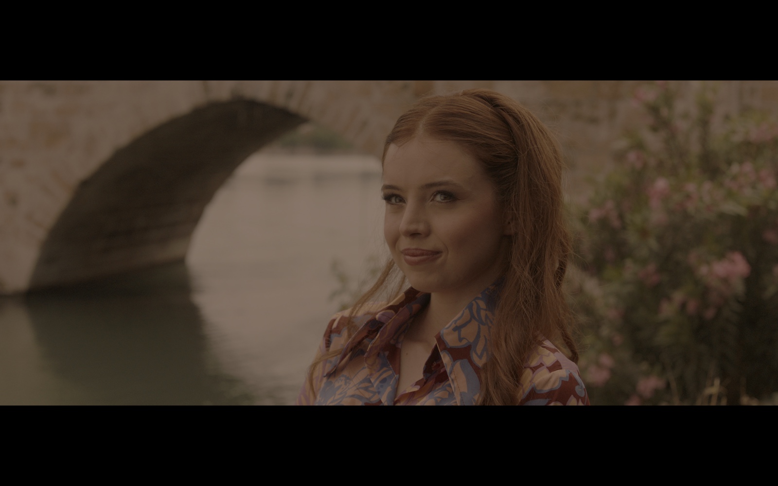 Radyo Günleri — A woman beside the river with a stone bridge behind her.