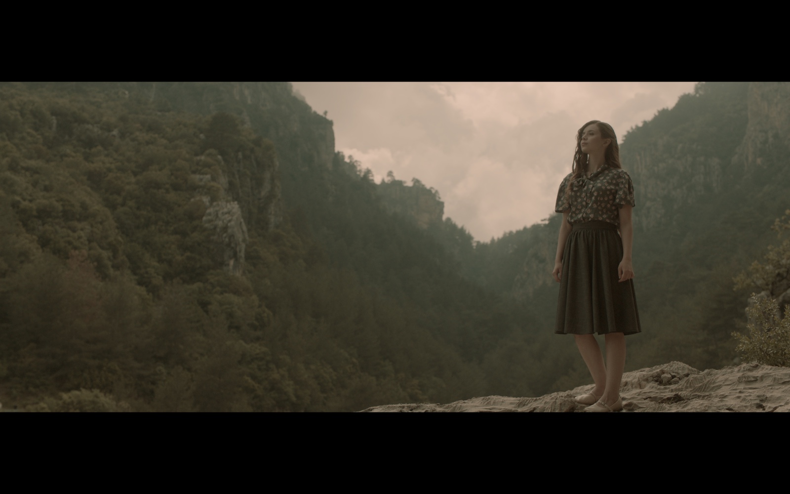 Radyo Günleri — A woman standing on a rocky ledge above a forested valley.